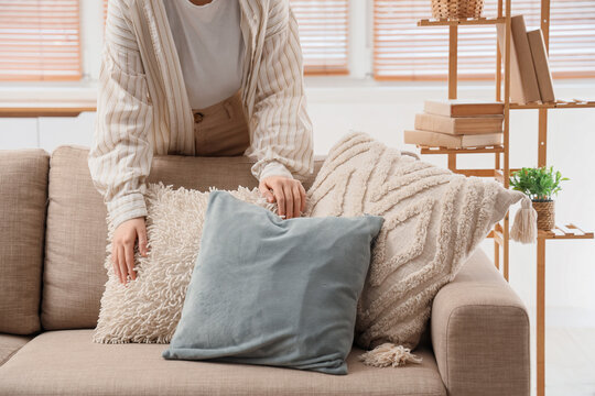 Young woman fluffing pillows on cozy sofa in living room