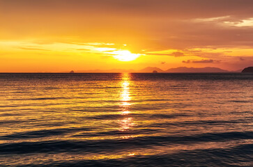 Obraz premium Bright and colorful sunset over the ocean with intense orange tones and shimmering water surface. Ideal tropical travel background with romantic and warm evening atmosphere.