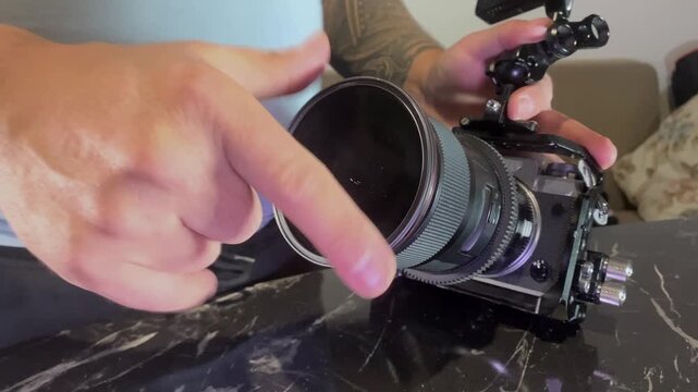 Hands screwing ND filter onto camera lens close-up, adjusting light reduction for controlled exposure, improving image quality during filming and photography in bright outdoor shooting conditions
