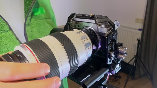 Hands installing telephoto lens via adapter on camera close-up, attaching long focal length optic to mirrorless body, demonstrating mounting process for photography, video production equipment setup