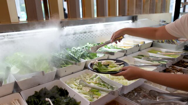 Customer Selecting Fresh Vegetables at a Steaming Asian Buffet Salad Bar