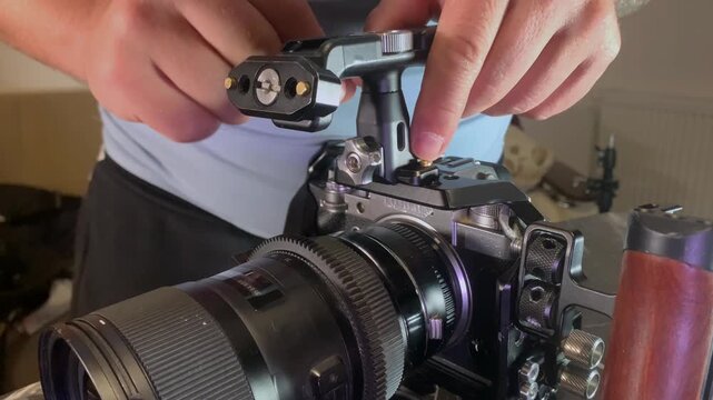 Hands removing handle from camera cage close-up, loosening mount and detaching top grip from rig system, reconfiguring filming equipment for different shooting setup, technical adjustment