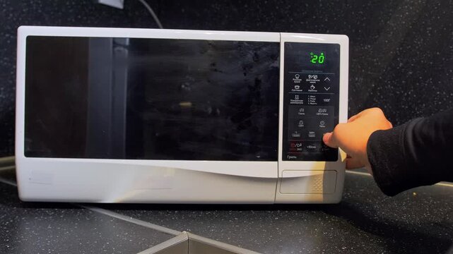 hand selecting microwave program close-up shot on control panel with finger pressing buttons, kitchen appliance operation showing cooking mode setup and timer adjustment in modern home environment