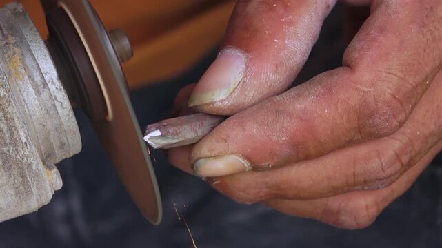 Vivid sparks fly as a worker uses a spinning grinding wheel to sharpen the tip of a metal tool bit in a workshop.