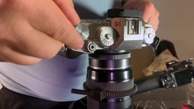 Hands turning camera exposure control knob close-up, adjusting settings on vintage style camera body, fine tuning brightness for accurate image capture, technical control in photography workflow
