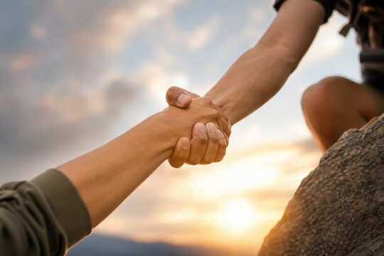 Two hands clasp together in a gesture of support against a scenic backdrop, symbolizing teamwork and connection during an outdoor adventure.