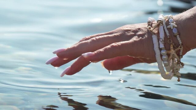 Hand Water Ripples Fingers touch clear turquoise lake surface wearing summer shell bracelets on a bright sunny day