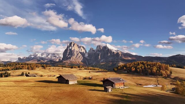 A stunning drone view of the Sassolungo, Langkofel mountain group in the Dolomites. Majestic alpine peaks covered with light snow glow in the warm evening sunlight, surrounded by autumn forest and gre