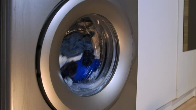 washing machine rinsing clothes close-up front view with drum rotating and water circulating, laundry process scene showing fabric cleaning stage during wash cycle in modern home appliance