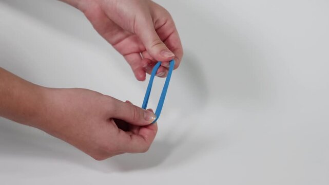 Hands stretching a blue elastic band by pulling both ends apart and releasing.