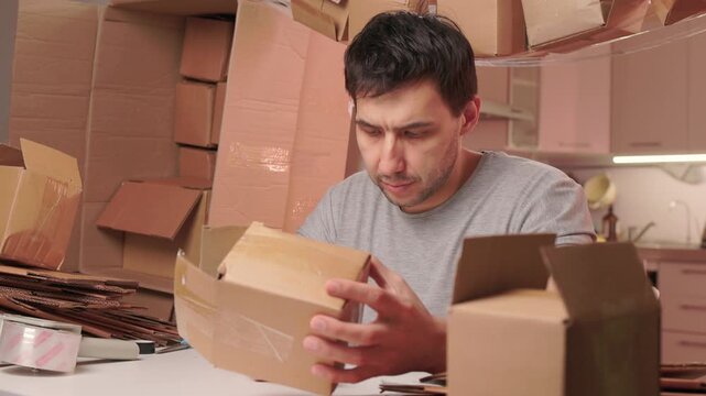 Man packs swiftly. Worker rapidly assembling and sealing packages at busy station. Energetic individual quickly folding and locking tabs on cardboard boxes for shipping