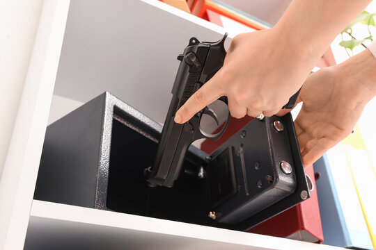 Woman putting pistol into safe on shelf in office, closeup