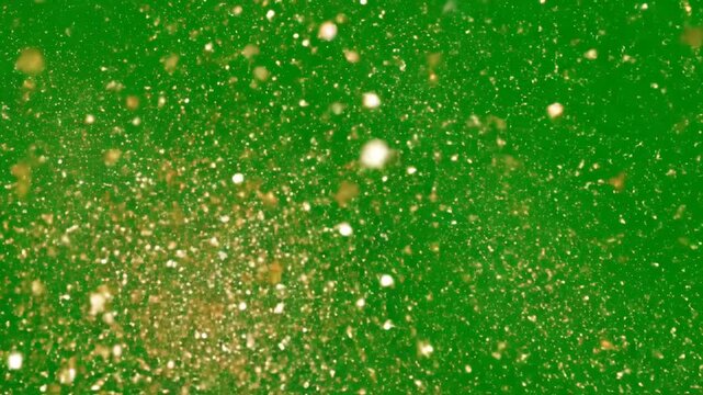 Golden glitter particles explode and spread on a green screen, creating a dazzling effect for overlays and special effects.