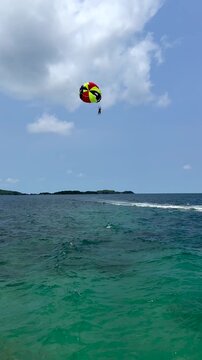 Parasailing over tropical sea with speedboat, aerial water sport, summer vacation adventure. Person parasailing above turquoise tropical sea, pulled by a speedboat.