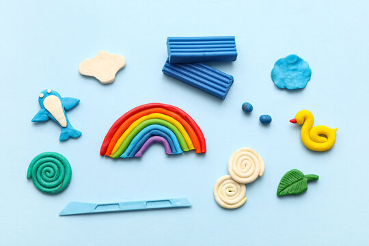 Colorful modeling clay figures with rainbow, dolphin, duck, clouds and sculpting tool on blue background, children's creativity, diy craft activity, playful handmade composition