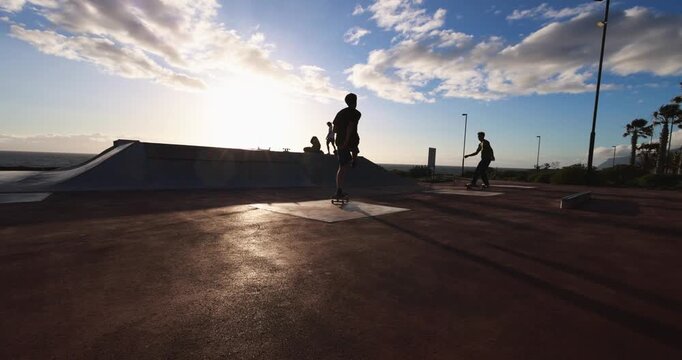Teenager people having fun at skateboard park outdoor during sunset time - Summer lifestyle, skaters and extreme sport concept - UGC wide lens content
