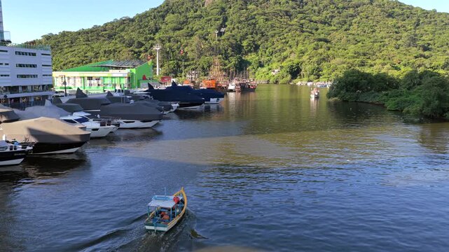 A boat travels through a marina surrounded by covered yachts and green hills in Balne&aacute;rio Cambori&uacute;, Brazil. Ideal for travel or maritime content.