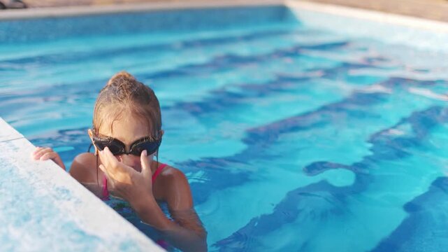 A girl in a bright swimsuit with swimming goggles dives into a pool with clear transparent water