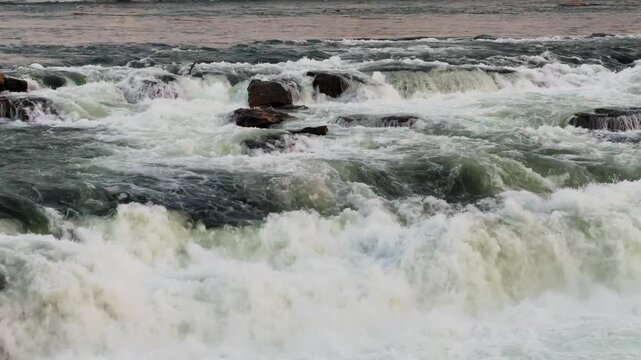 Close-up view of turbulent river rapids crashing over rocks with foamy white water and strong currents, capturing powerful natural motion in an outdoor setting