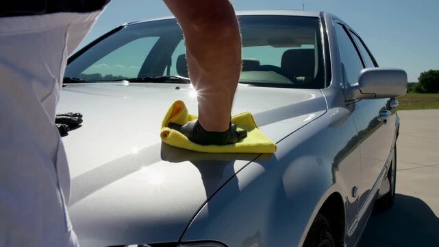 Meticulously buffing a lustrous silver sedan's hood to achieve a brilliant, pristine shine on a beautiful clear day