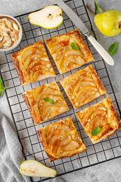 Pear puff pastry pie with caramel sauce and almond on a gray concrete background. Delicious pie.