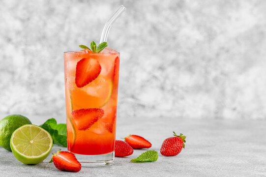 Glass of strawberry lemonade with lime slices and mint leaves. Cold summer drink. Copy space.