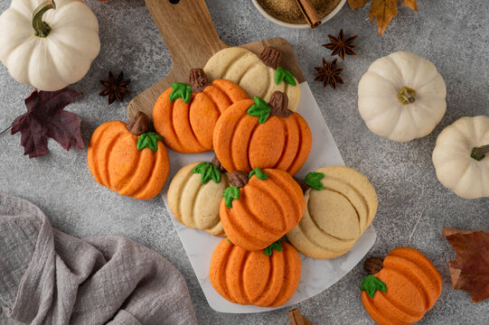 Themed dessert for Thanksgiving. Spiced cookies in the shape of white and orange pumpkins on a wooden board on a dark wooden background. Top view, copy space.