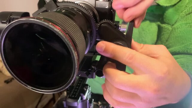 Hands installing manual focus motor on camera stabilizer close-up, attaching control unit to lens system, preparing professional filming equipment for precise focus control in video production