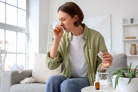 Allergic young woman with pills sneezing at home