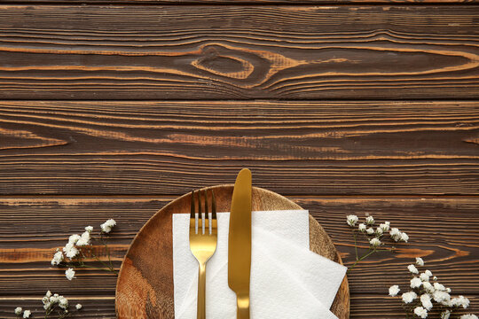 Plate with cutlery, paper napkins and gypsophila flowers on wooden background