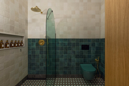 Modern bathroom interior with two-tone tiled walls, a glass shower partition, and contemporary fixtures including a toilet and shower head