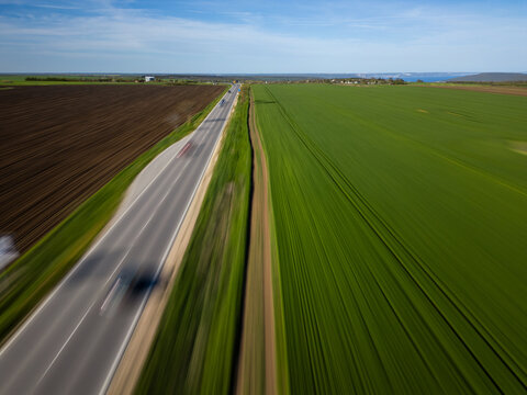 Fast motion blur aerial view of highway through green agricultural fields