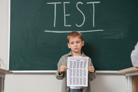 Sad schoolboy with results of test in classroom