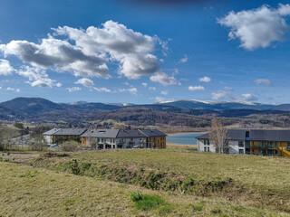 Fototapeta premium Landscape view of modern holiday houses near lake under blue sky with clouds. Concept of travel destination, eco tourism, peaceful retreat, nature and architecture.