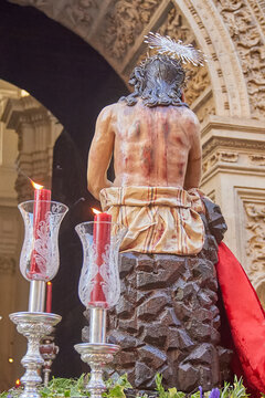Rear view of a sculpture of Jesus Christ with visible wounds on a processional platform during a Catholic ceremony, expressing suffering, devotion and religious symbolism