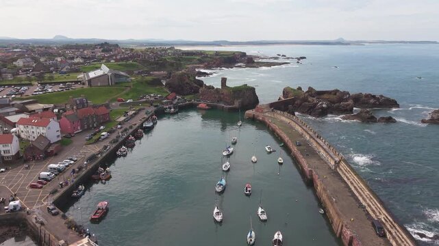 Aerial view of a traditional stone harbor and ancient castle ruins on the rocky coast, Scotland.
