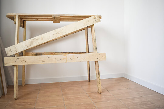 Wooden construction sawhorses made of timber planks standing on a tiled floor in a white empty room