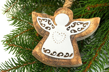Fototapeta premium Wooden angel ornament hangs on green pine branches during winter holiday season