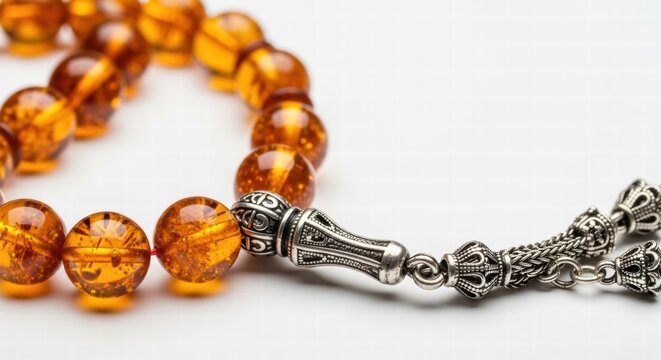 Close-up of amber prayer beads with intricate silver details on a white background