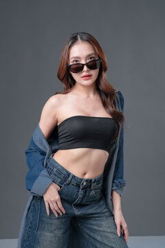 Beautiful Asian woman in denim shirt and black tube top smiling, young fashionable female posing in jeans on grey background