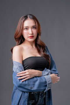 Beautiful Asian woman in denim shirt and black tube top smiling, young fashionable female posing in jeans on grey background