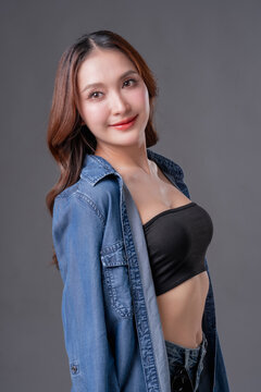 Beautiful Asian woman in denim shirt and black tube top smiling, young fashionable female posing in jeans on grey background