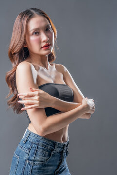 Beautiful Asian woman with glowing skin and brown hair, professional beauty portrait of young female in black tube top on grey background