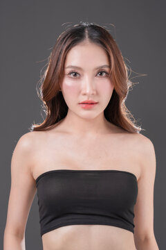 Beautiful Asian woman with glowing skin and brown hair, professional beauty portrait of young female in black tube top on grey background