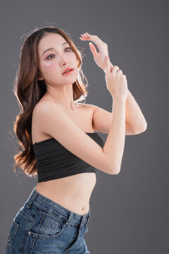 Beautiful Asian woman with healthy skin and long wavy hair smiling, glowing skin and beauty portrait of young female on grey background