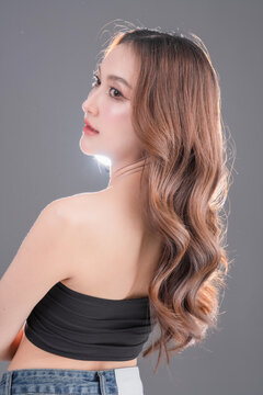 Beautiful Asian woman with healthy skin and long wavy hair smiling, glowing skin and beauty portrait of young female on grey background