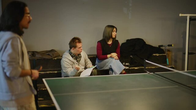 Students are actively engaged in a game of table tennis while others watch and learn. This scene highlights youth participation in sports and inclusive recreational activities.