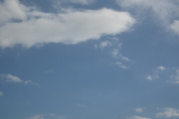 Fototapeta premium A clear blue sky with soft white clouds scattered across the frame. Minimalist natural background with plenty of copy space, ideal for weather, freedom, calm, and environmental concepts.