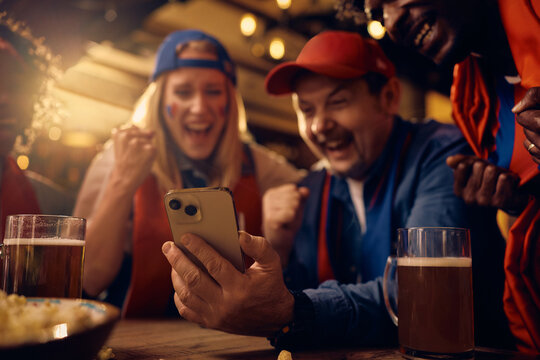 Close up of supporters cheering while watching sports match on mobile phone in pub.