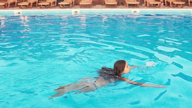 Girl in leopard swimsuit playing in the pool under the summer sun